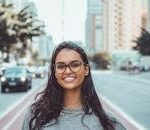 A young woman with glasses smiling on a city street, embracing urban lifestyle.