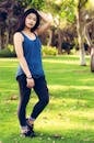A stylish young woman stands confidently in a lush Dubai park under the sun.